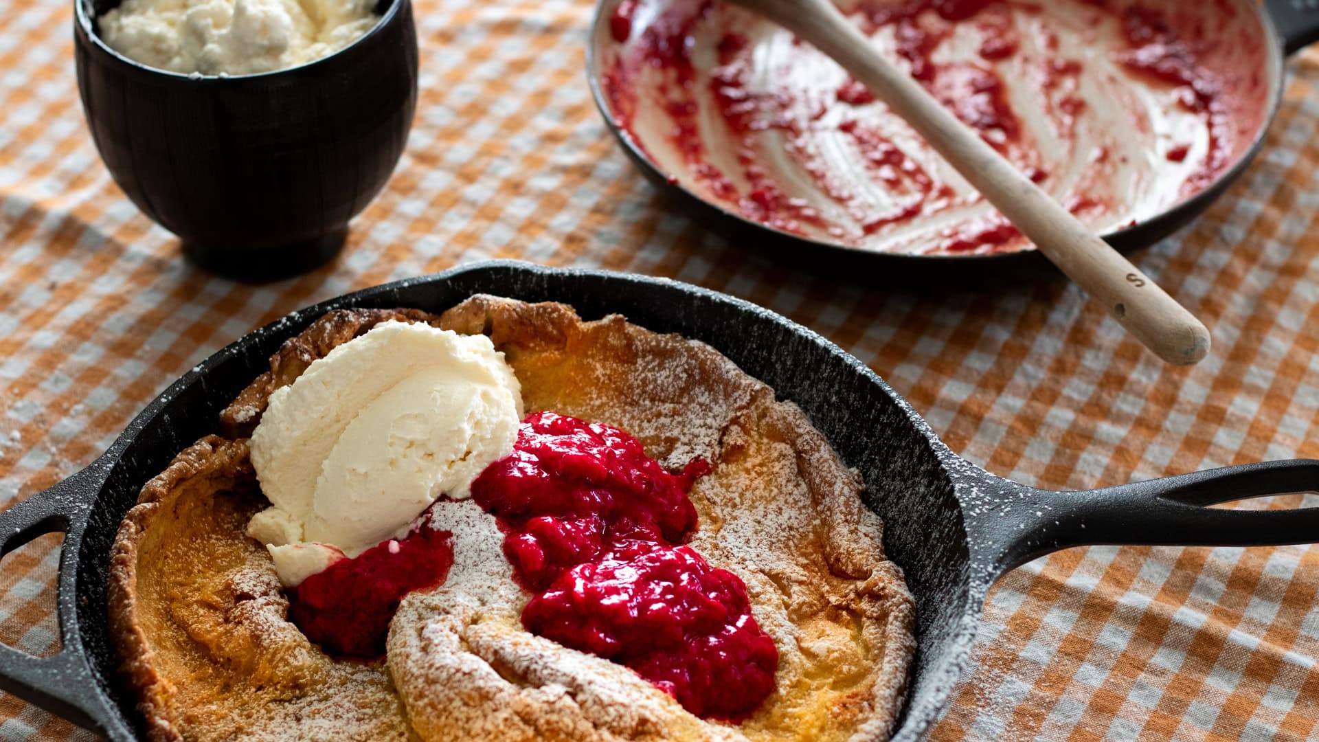 dutch baby served in a pan on a table with jam and whipped cream