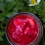 open jar of red homemade jam in garden bed