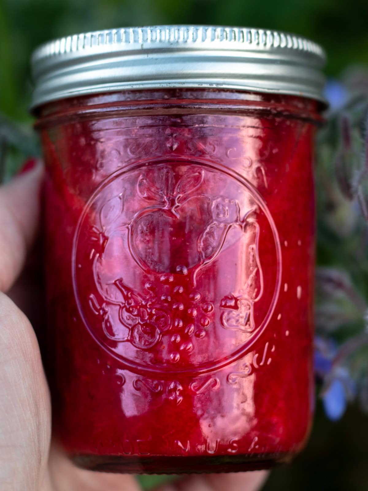 woman's hand holding a jar of red homemade jam