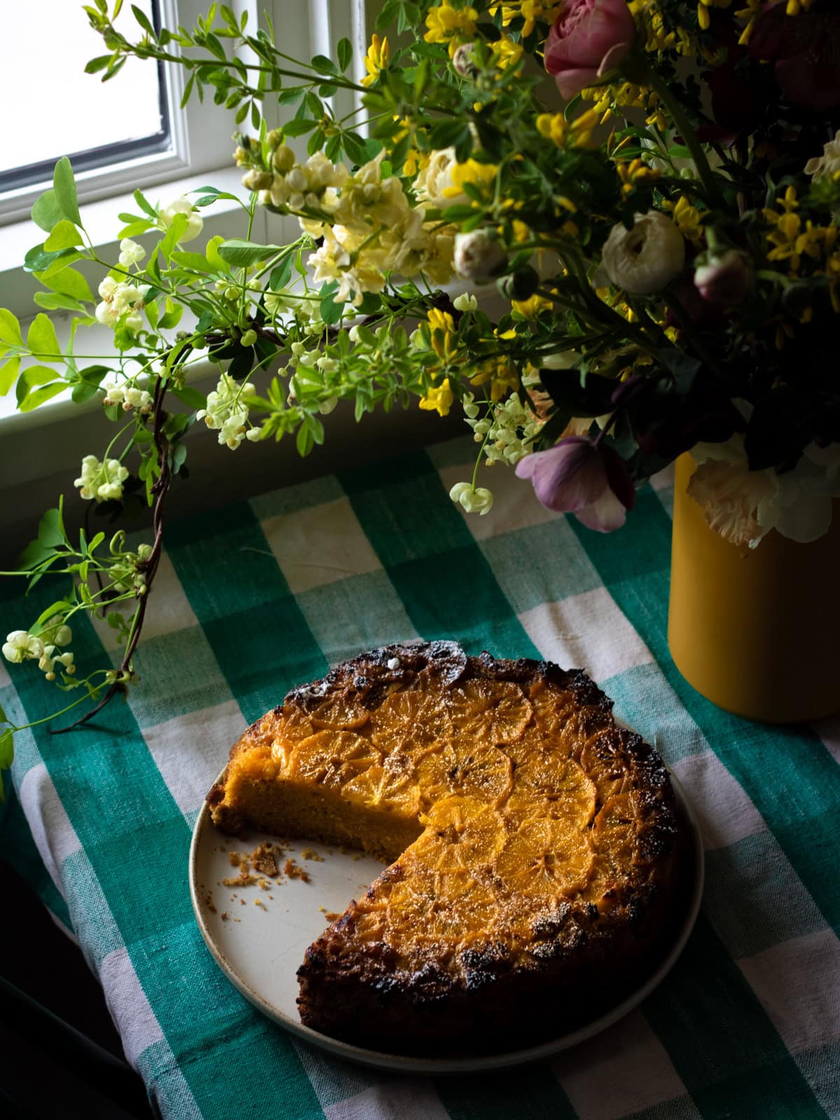 cake with lemon slices on top sitting on a table by the window with boquet of flowers nearby